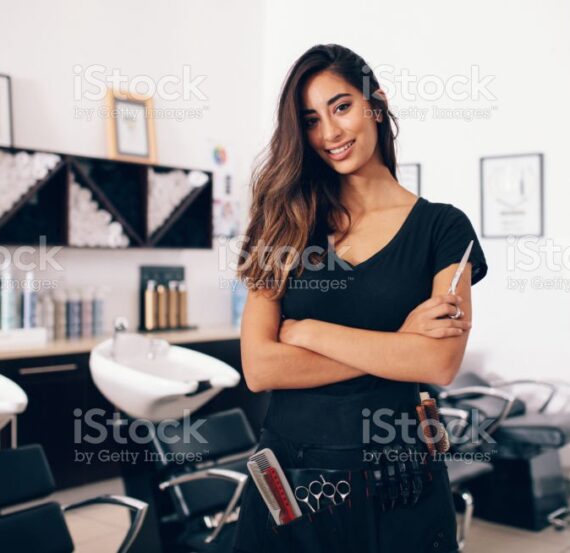Female hairdresser in salon holding scissors in hand. Smiling young hairdresser standing in salon.
